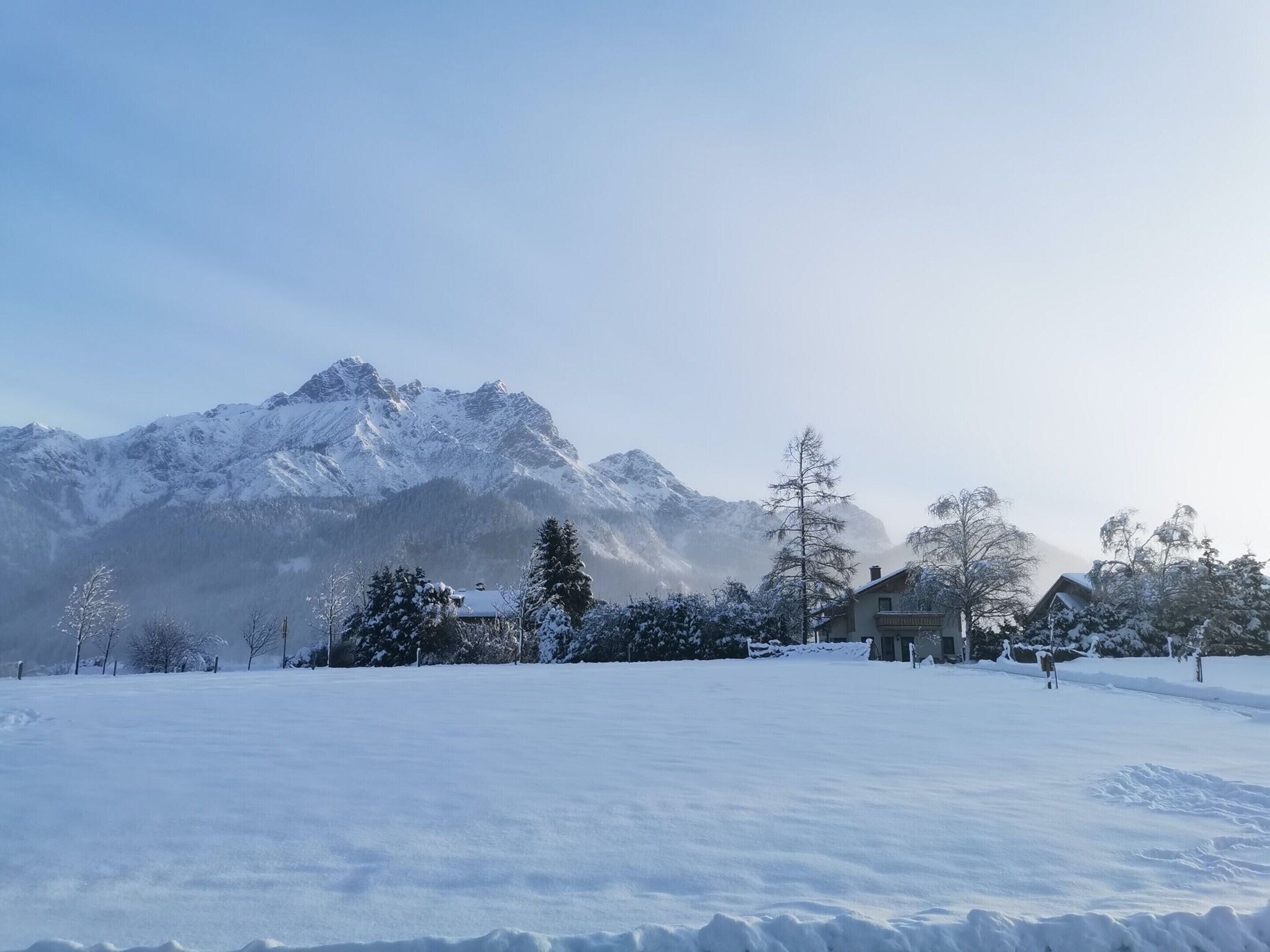 A snow-covered landscape with a mountain range in the background and a building with a balcony in the foreground.