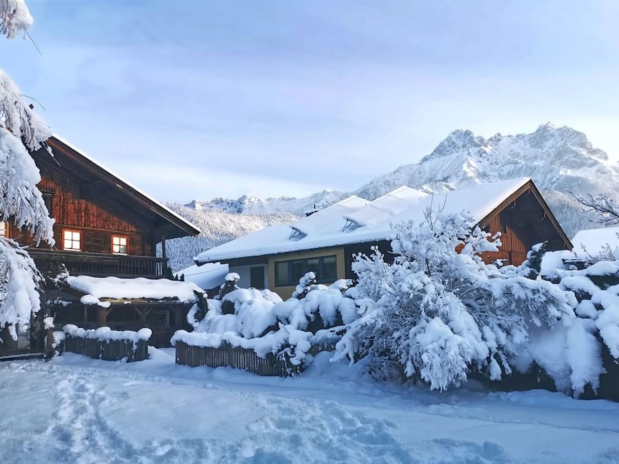 A wooden cabin with a snow-covered roof and a mountain backdrop.
