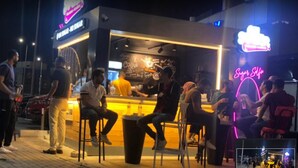 An outdoor café with a counter and stools, surrounded by people. - Local Style Khan El Khalili Decoration Living Room (Cairo)