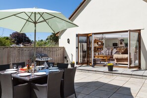 An outdoor dining area with wicker furniture, a large umbrella, and a grill. - The Garden Apartment a Luxurious Rural Retreat (Wellington)