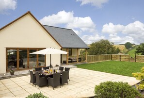 A patio area with a table and chairs, a large umbrella, and a view of the surrounding landscape. - The Garden Apartment a Luxurious Rural Retreat (Wellington)