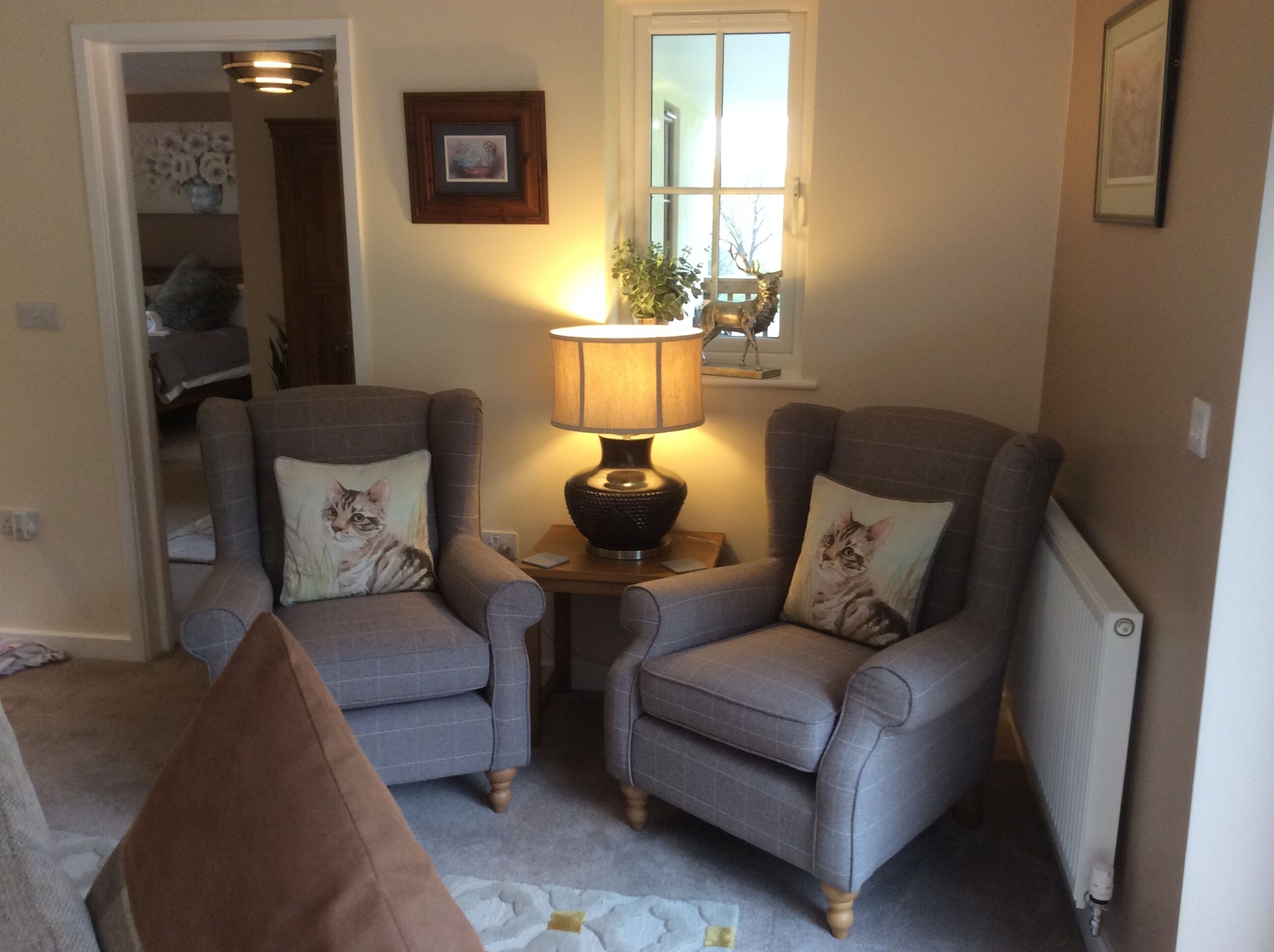 A cozy living room with two armchairs, a table with a lamp, a window with a view, and a radiator.