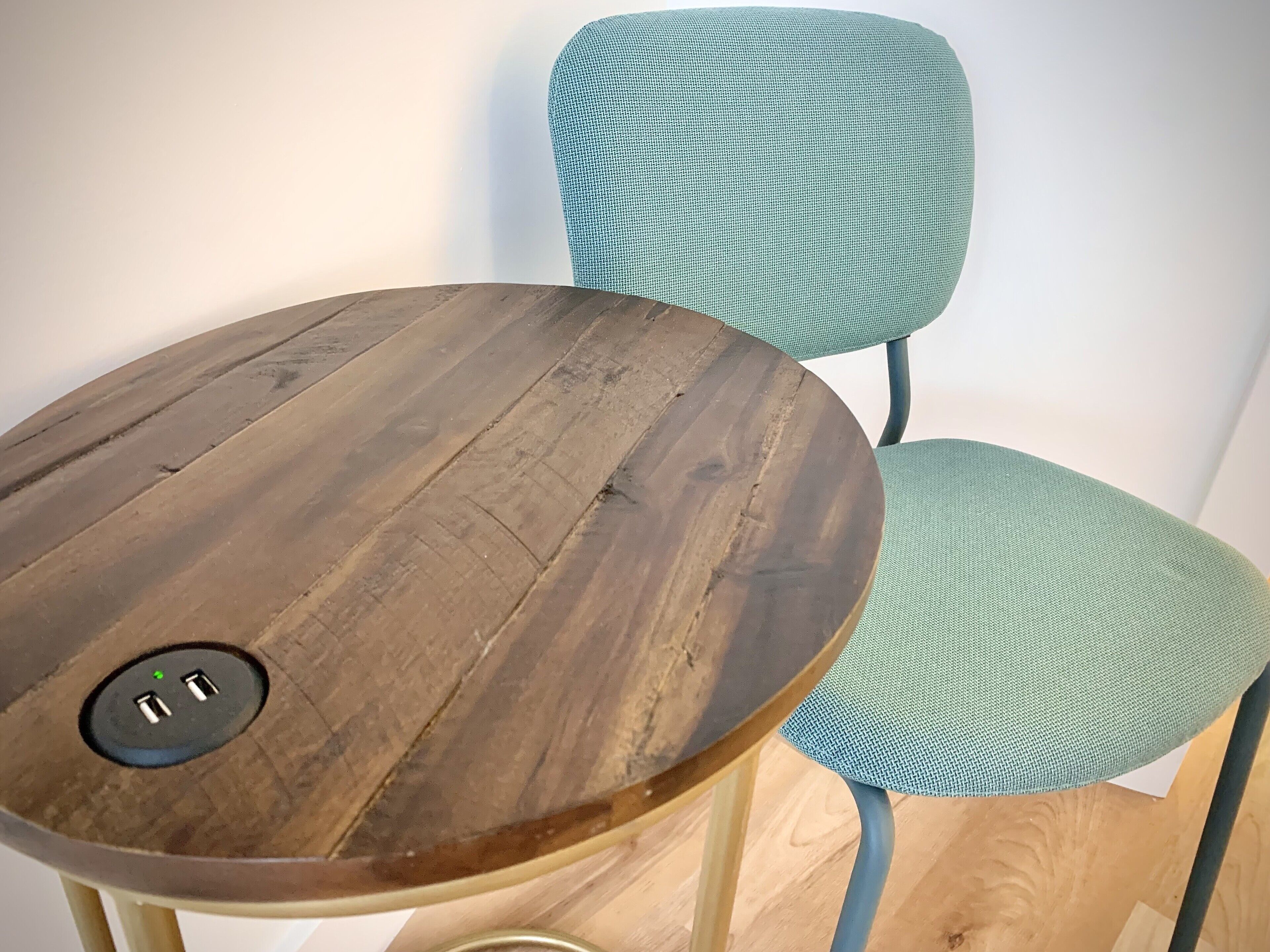 A round wooden table with a power outlet and a blue chair with a checkered pattern.