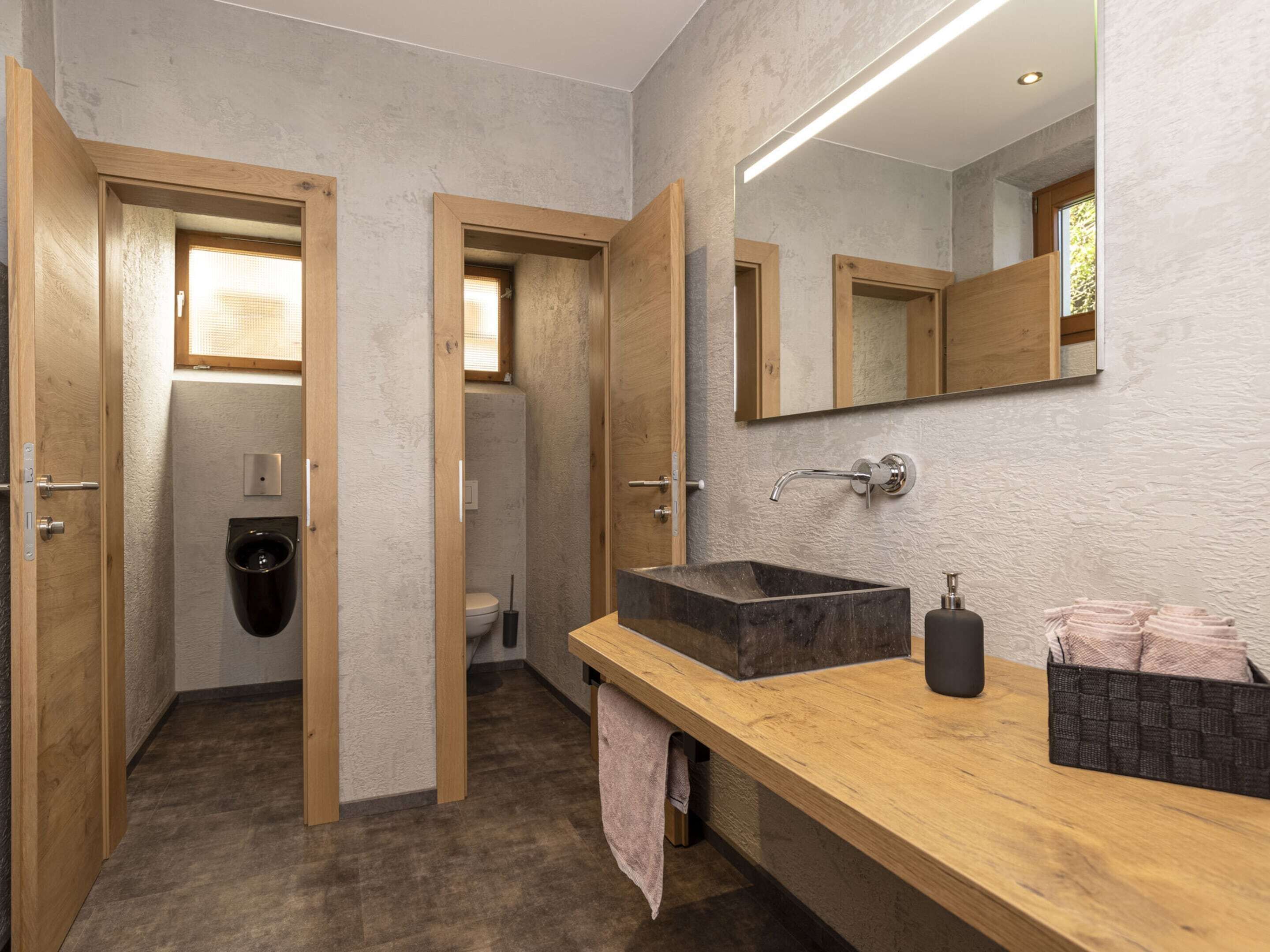 A modern bathroom with a wooden vanity, a large mirror, and a separate toilet area.