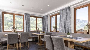 A modern dining area with grey upholstered seating, a wooden table, and large windows offering a view of a mountainous landscape. - Moiklerhof Holiday Home in Ramsau im Zillertal (Ramsau im Zillertal)