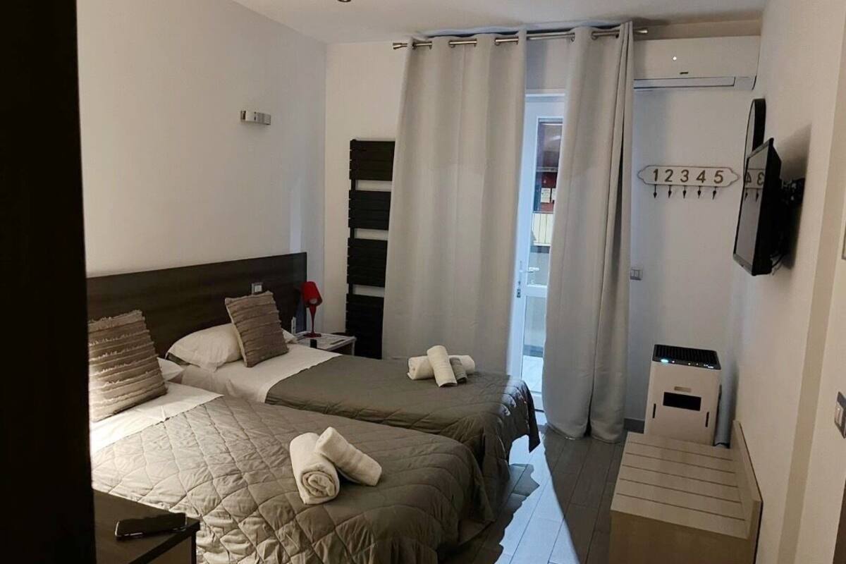Habitació d'hotel amb dos llits, un televisor fixat a la paret, un calefactor i una finestra amb cortines.