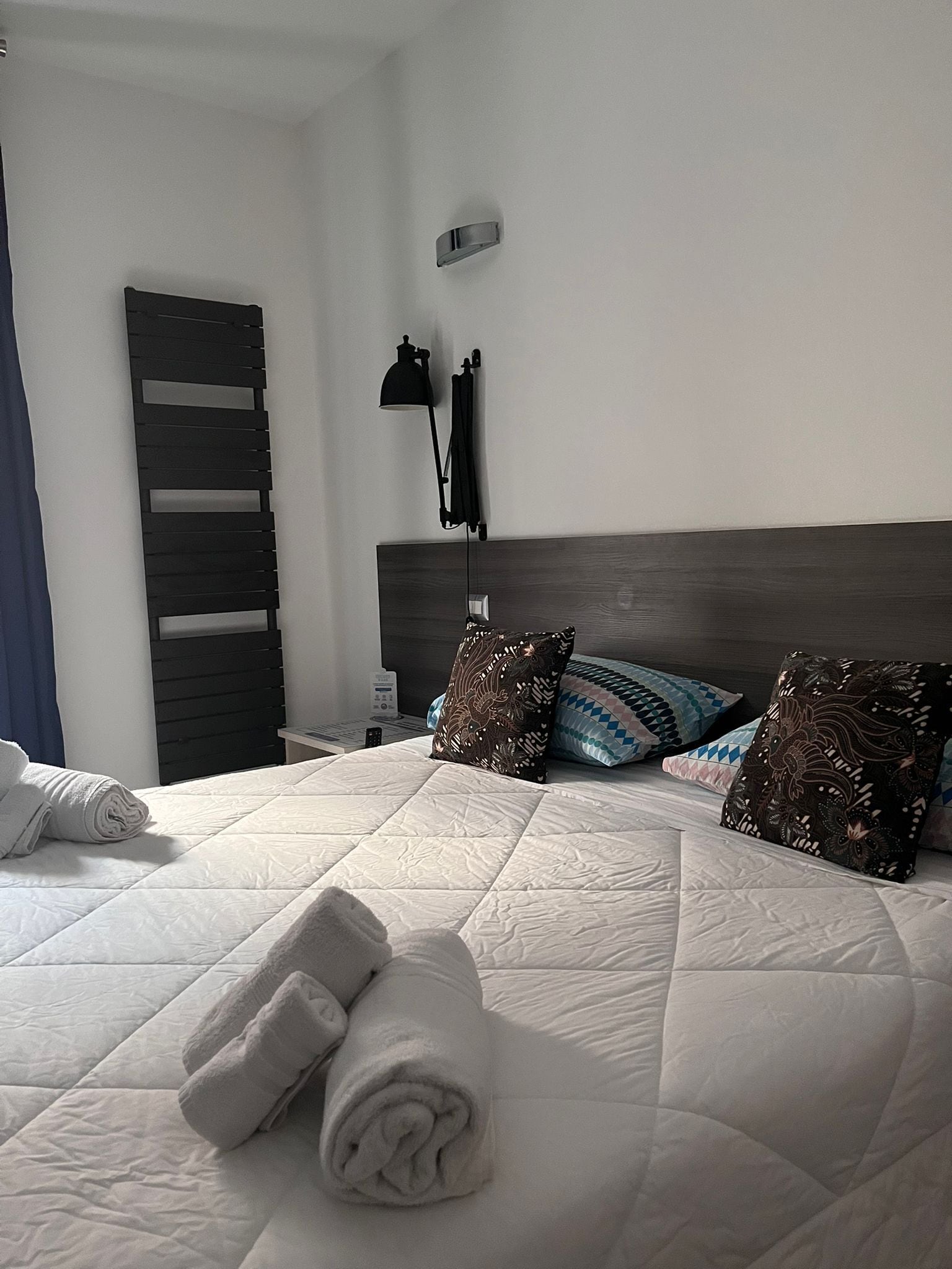 A neatly made bed with rolled towels, a bedside table with a lamp, and patterned pillows.