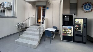 A small outdoor area with a vending machine, a table, and a chair.