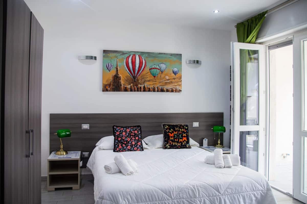 Habitació d'hotel moderna amb un llit gran, dos coixins, una tauleta de nit amb una làmpada i un quadre de globus aerostàtics a la paret.