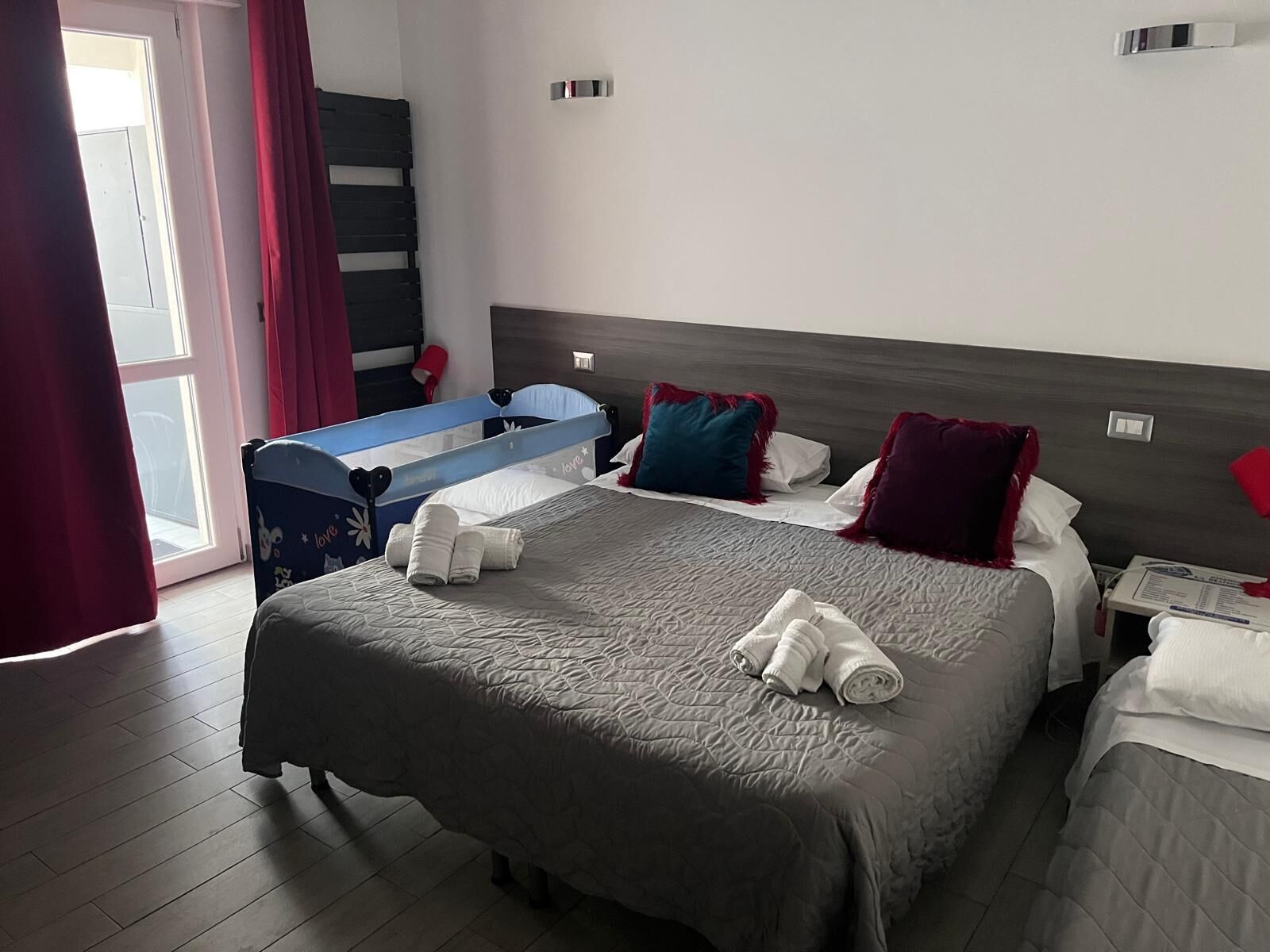 A hotel room with a large bed, a smaller bed, a desk with a chair, and a window with curtains.