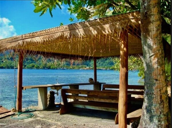 A wooden gazebo with a thatched roof overlooking a body of water, surrounded by trees.