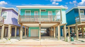Un edificio frente a la playa con balcón, pilares de madera y un letrero que dice 