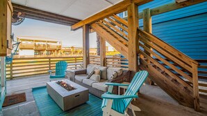 Un área de estar al aire libre con techo, una escalera de madera, un brasero y vistas a la playa.