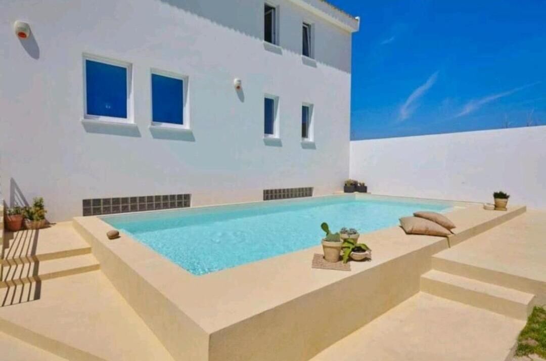 Edifici modern amb piscina, zona d'estar a l'aire lliure i plantes en testos.