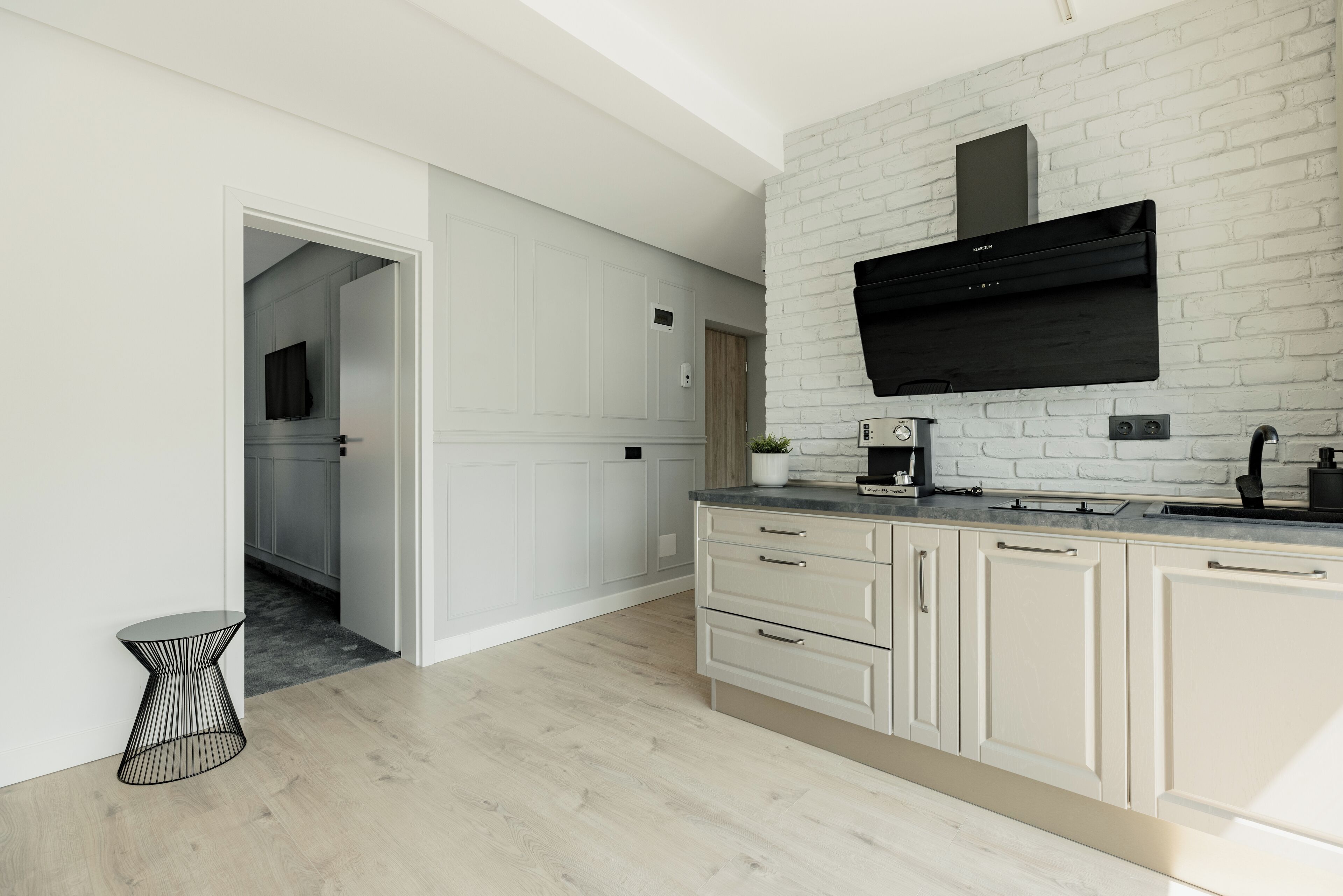 A modern kitchen with white cabinetry, a black range hood, and a small side table.