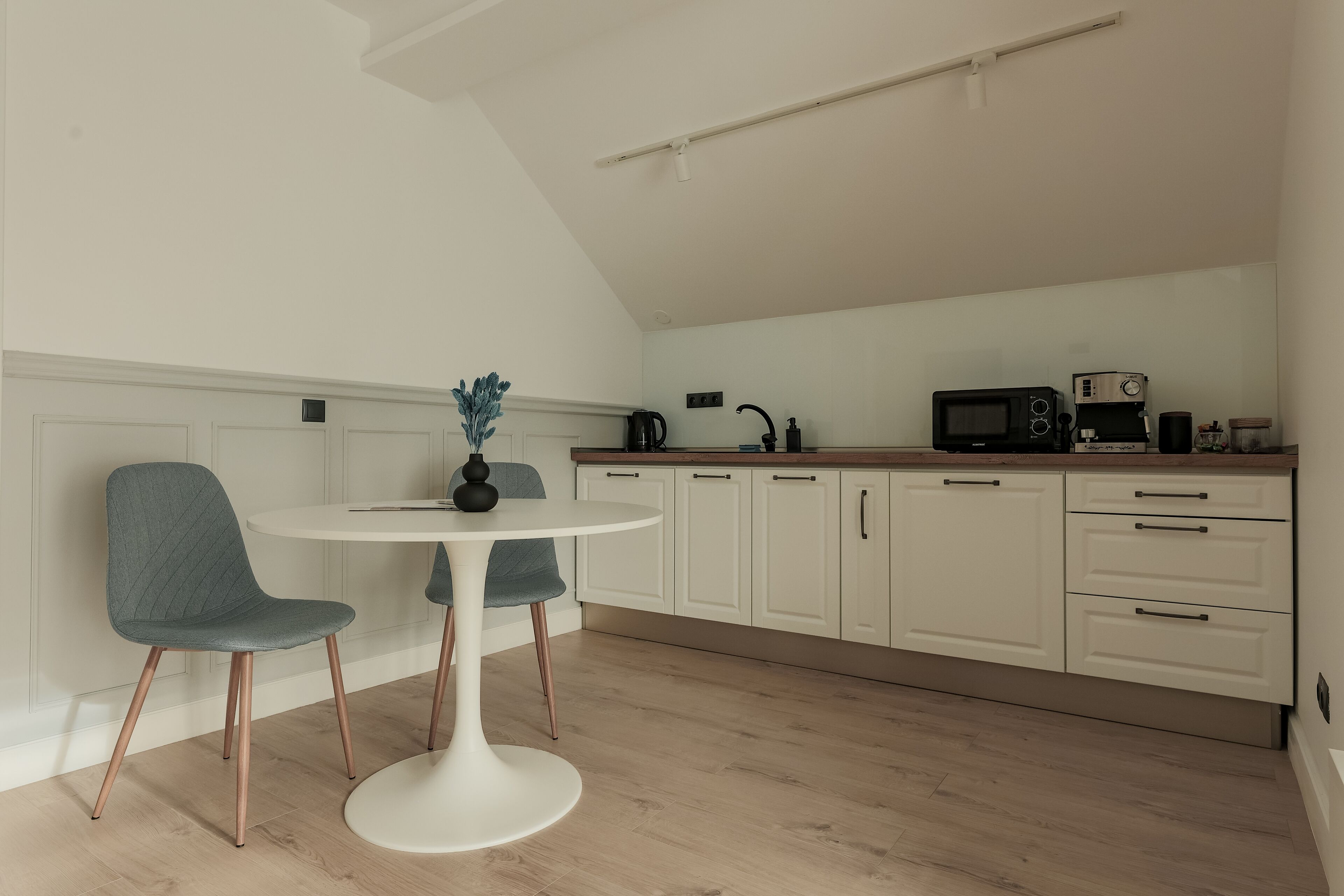 A modern kitchen with white cabinetry, a round dining table with two chairs, and a microwave on the countertop.