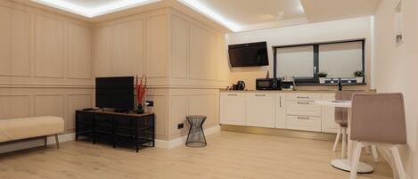 A modern kitchen with white cabinets, a flat-screen TV, and a dining area with a table and chairs.