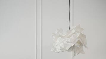 Un lit bien fait, avec une tête de lit grise et des oreillers blancs, une table de chevet et un luminaire fixé au mur.
