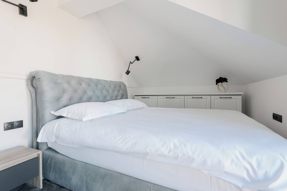 A neatly made bed in a modern bedroom with a tufted headboard, white bedding, and a small bedside table.