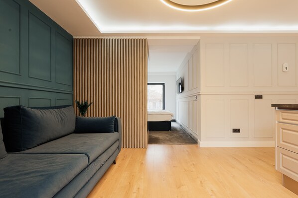 A modern living room with a grey sofa, wooden slatted partition, and a kitchen area with white cabinetry and a wooden countertop. - Nest Inn Meteor (Cluj-Napoca)