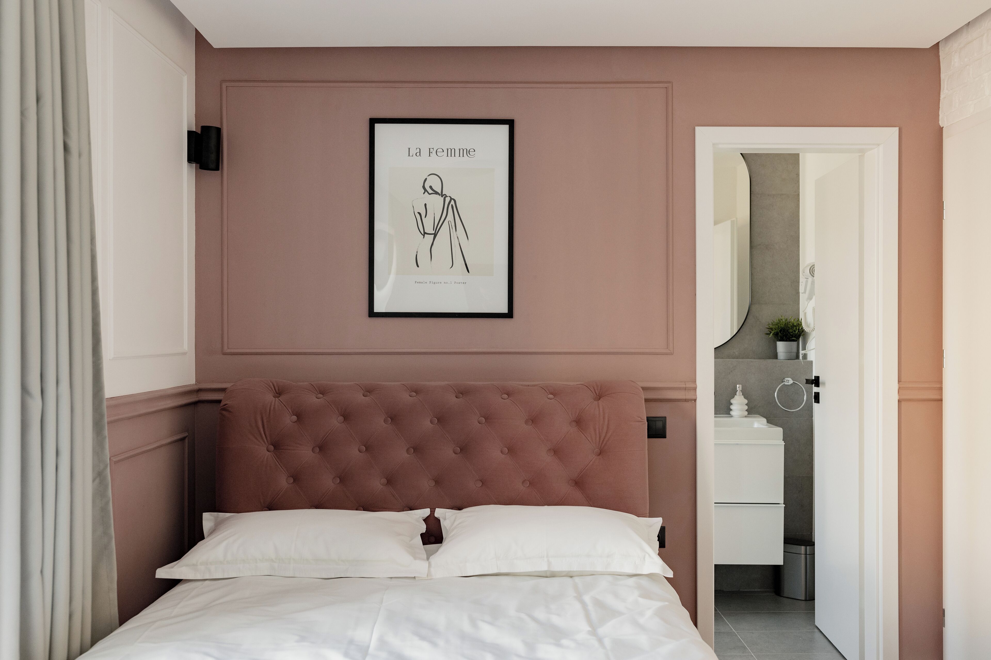 Ein Schlafzimmer mit einer gepolsterten Kopfstütze, einem gerahmten Kunstwerk an der Wand und Blick ins Badezimmer.