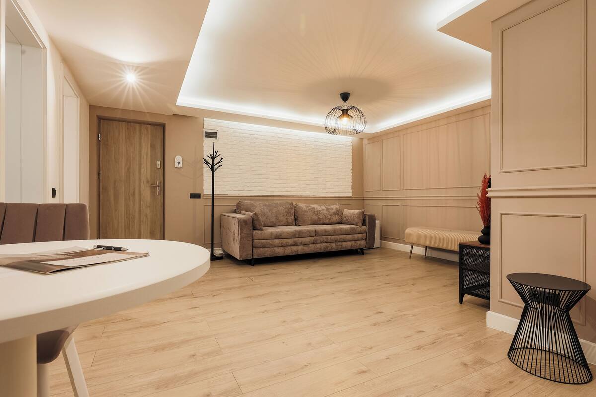 A modern living room with a round white table, a beige sofa, a black coffee table, and a unique black lamp.