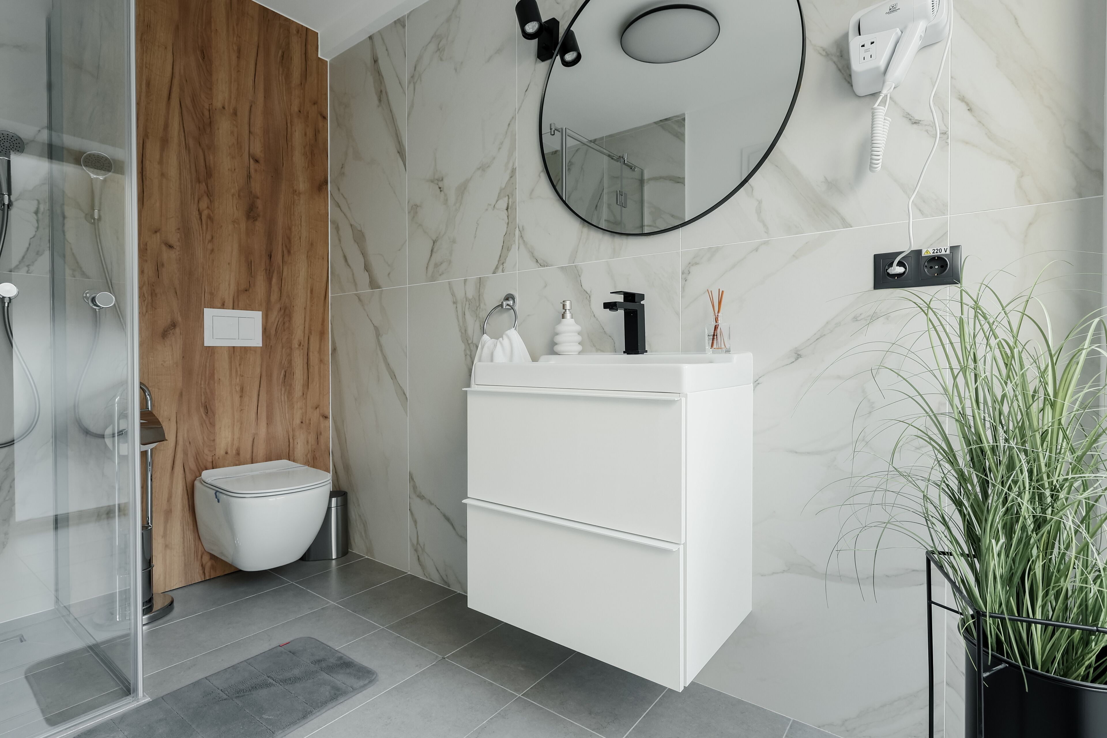 Un bagno moderno con parete rivestita in legno, un lavandino bianco con rubinetto nero, uno specchio e un asciugacapelli a parete.