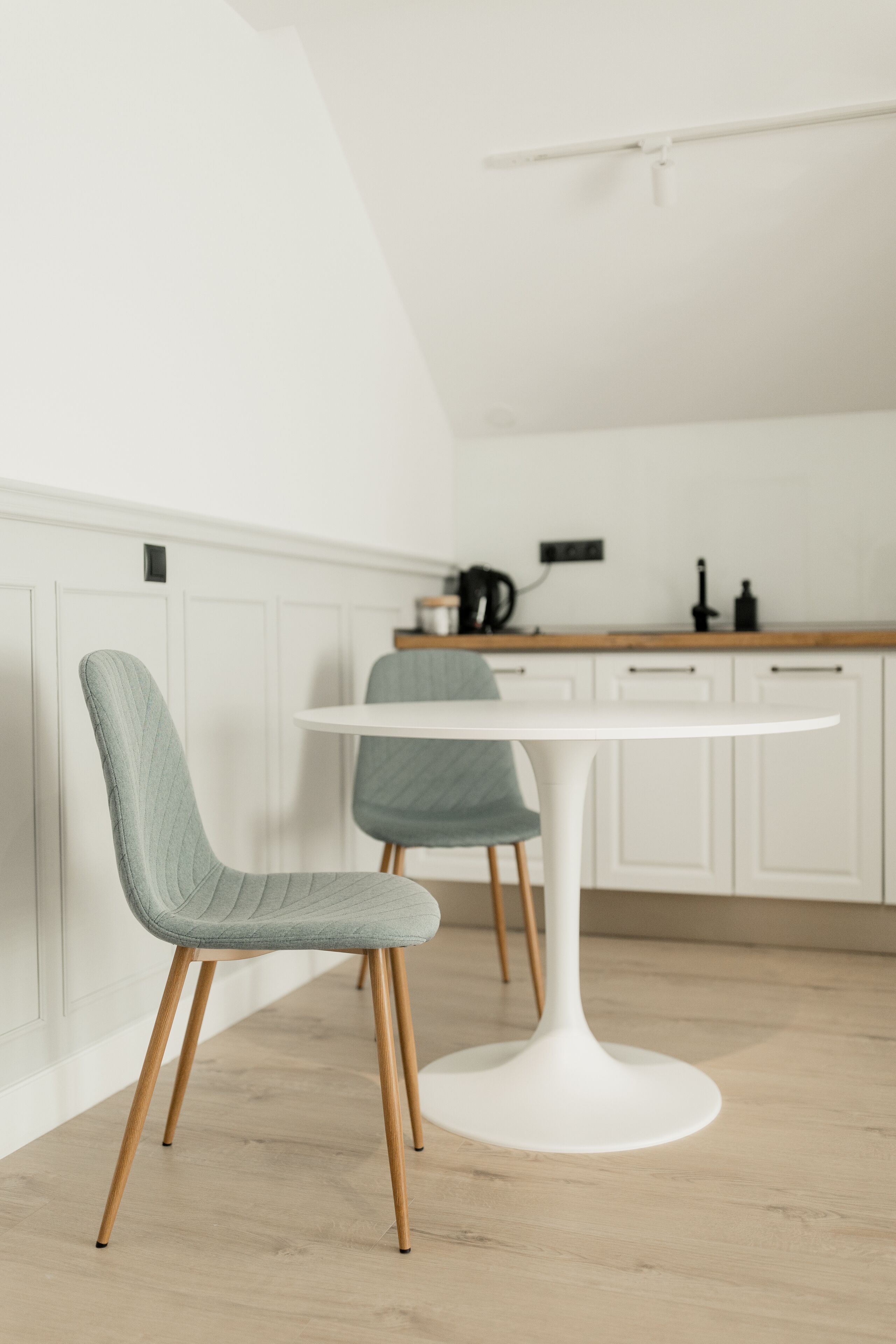 A modern kitchen with white cabinetry, a round white table, and two chairs with wooden legs.
