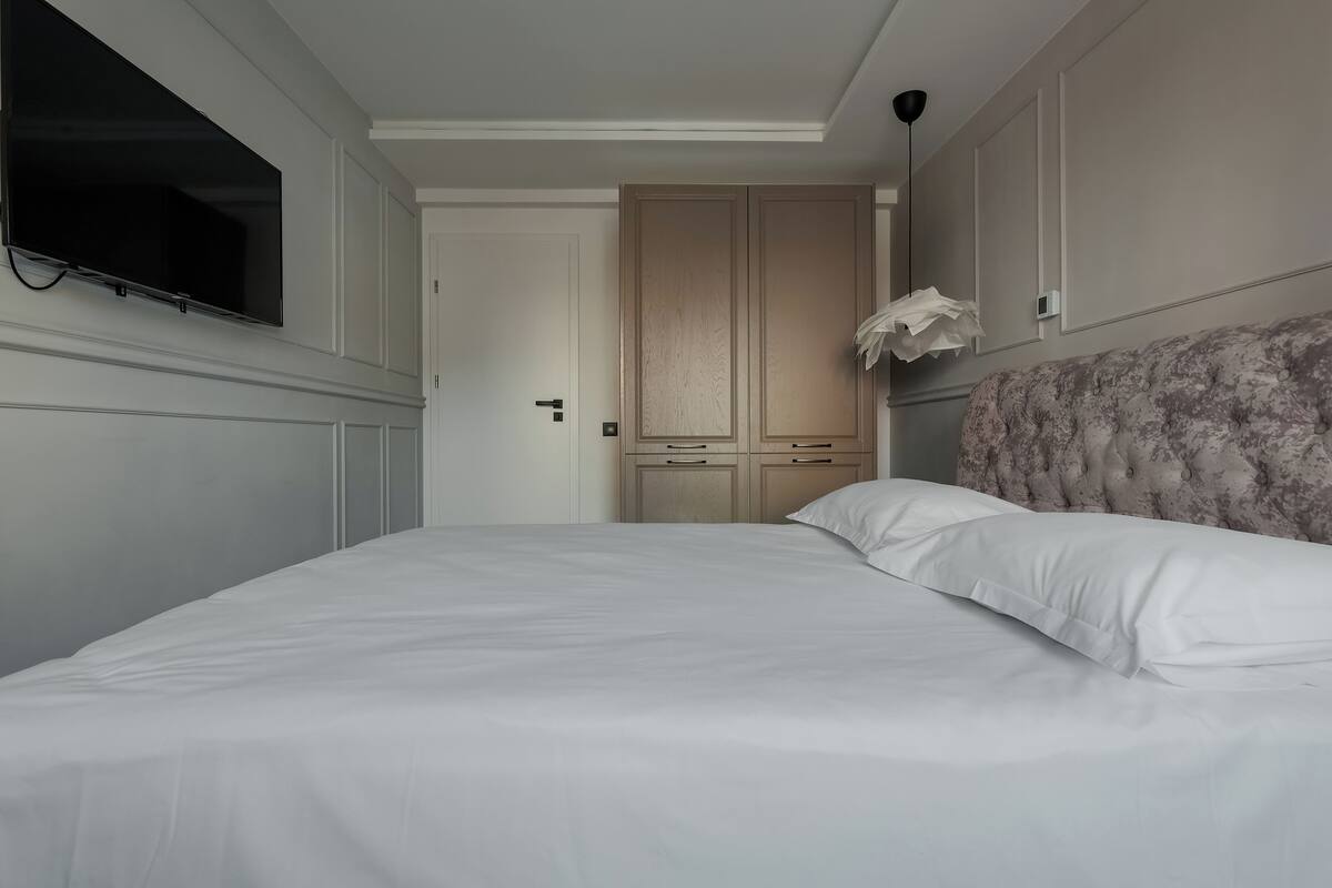 A bedroom with a bed, a television mounted on the wall, and a wardrobe.