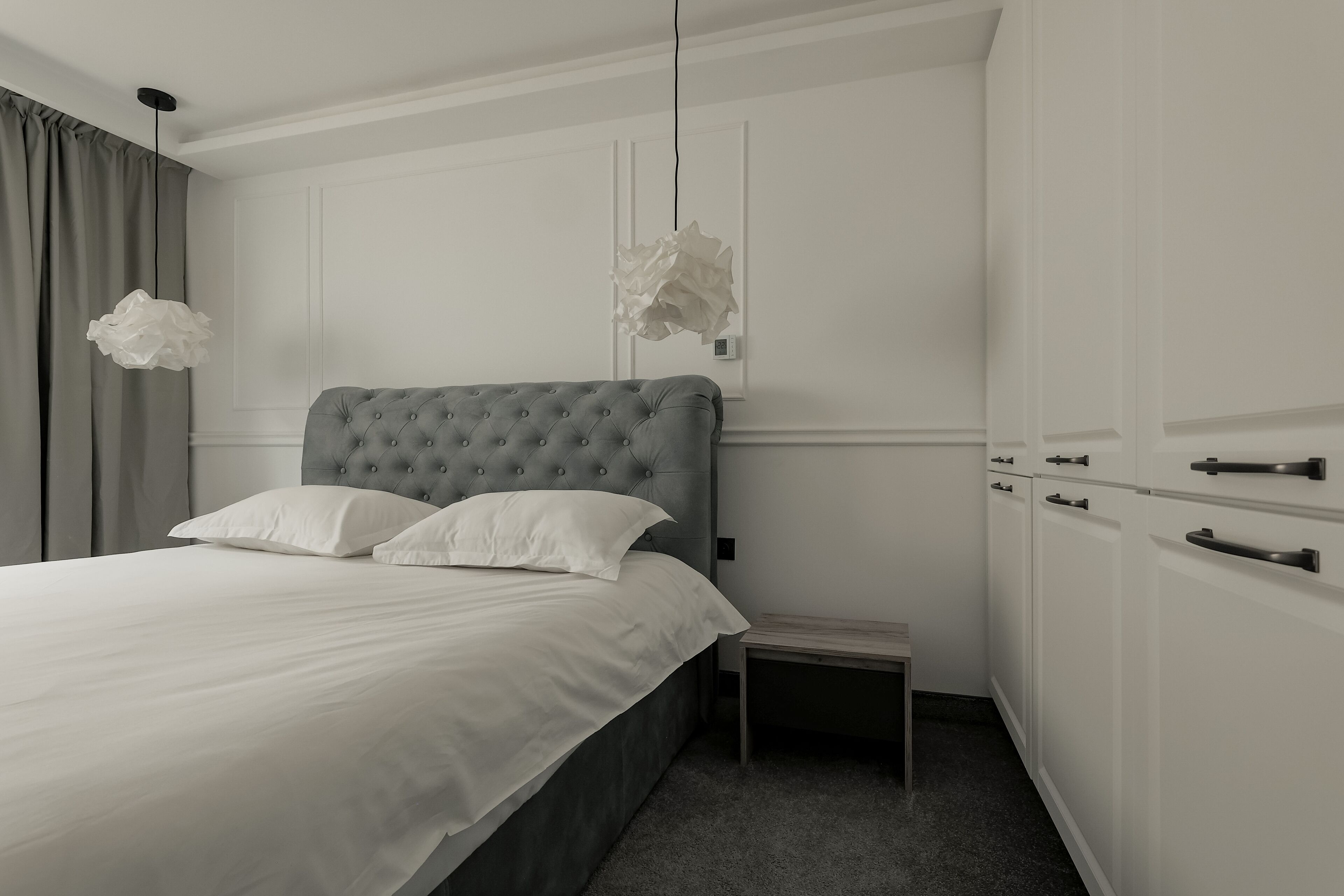 A neatly arranged bedroom with a tufted headboard bed, a bedside table, and a wardrobe with a handle.