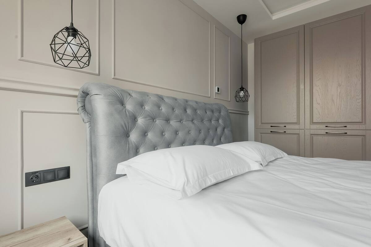 A bedroom with a tufted headboard, a bedside table, a hanging light fixture, and built-in cabinets.