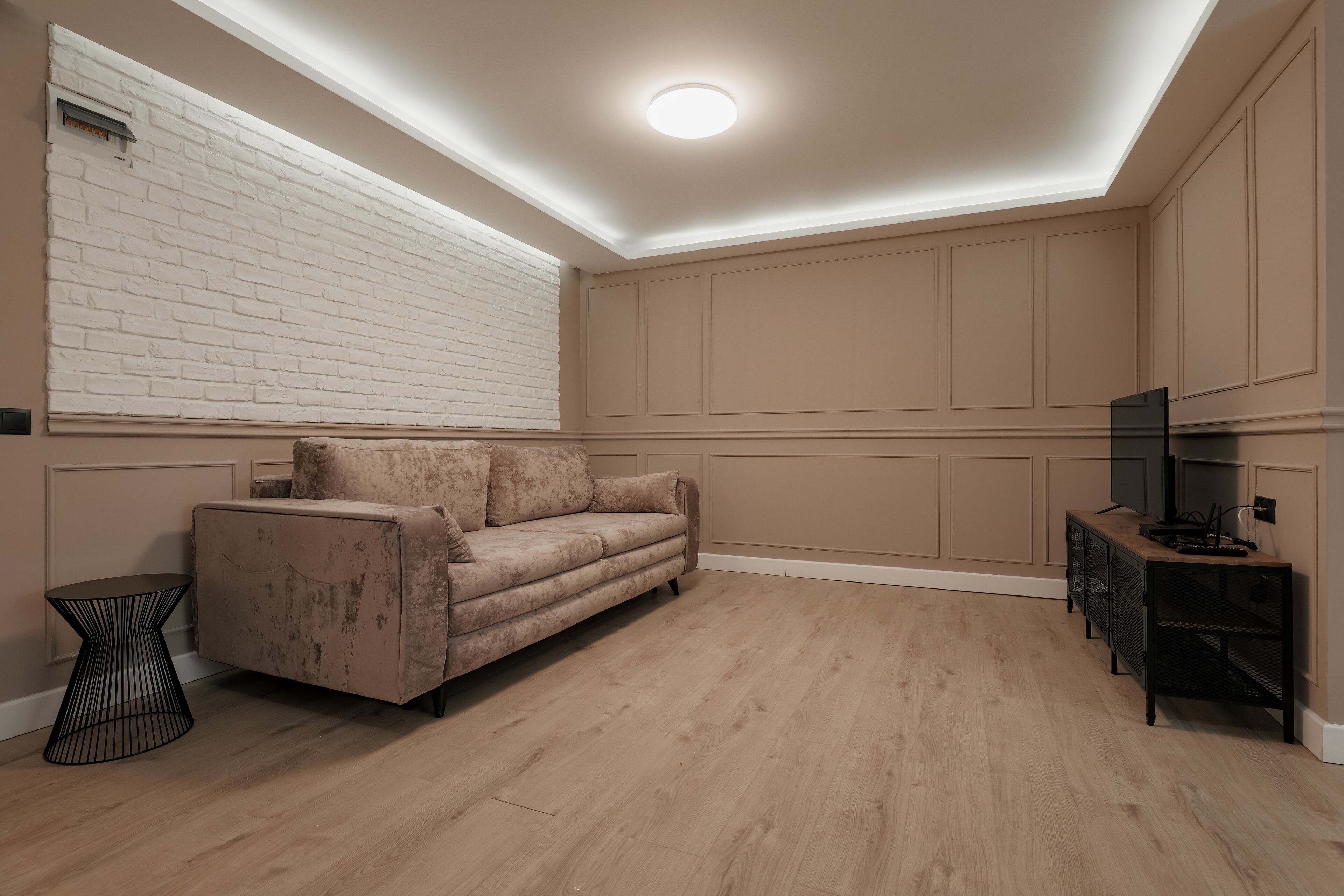 Una sala moderna con un sofá color beige, una mesita de noche negra y un mueble para televisión.