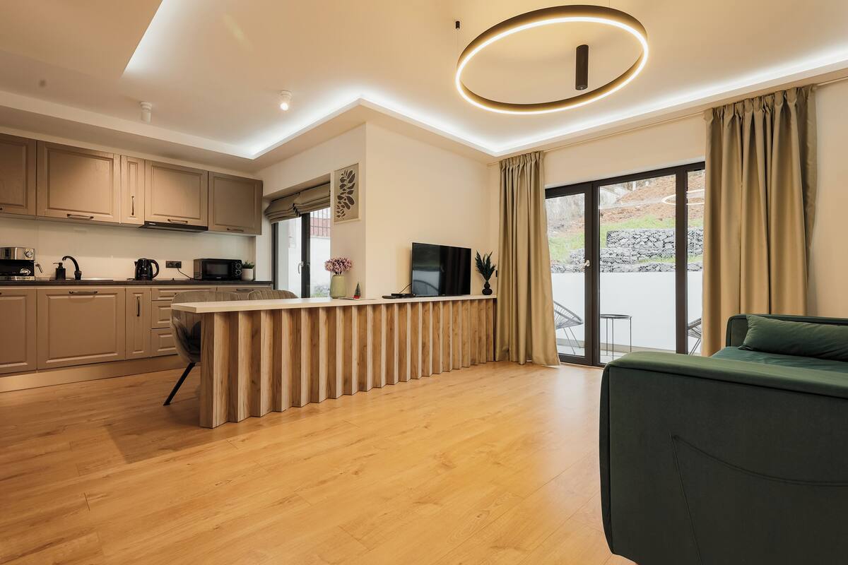 A modern kitchen with wooden cabinets, a central island, and a flat-screen TV.
