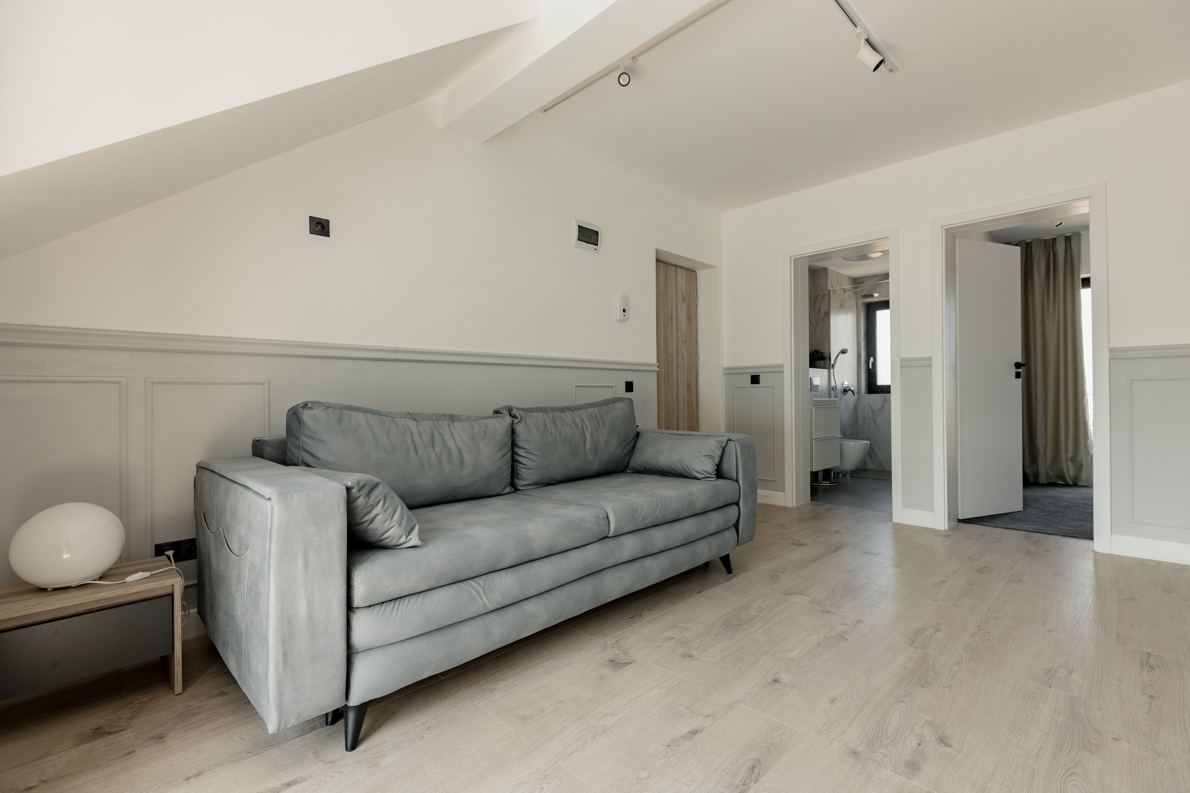 Un salón amplio con un sofá de cuero gris, un banco de madera y una lámpara esférica blanca.