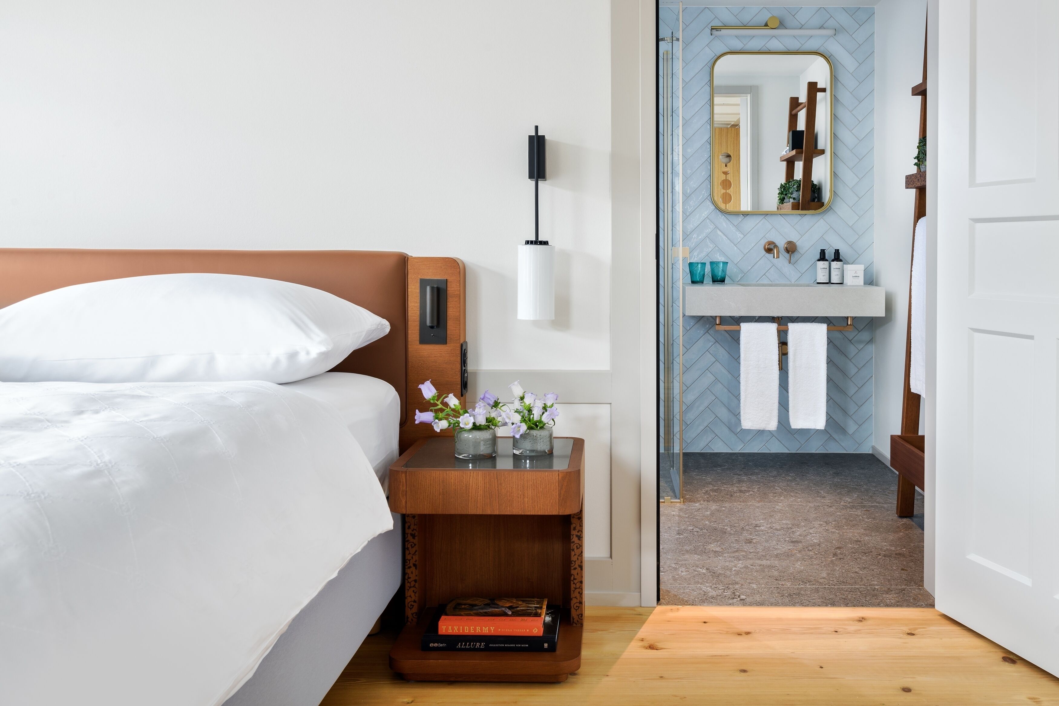Een slaapkamer met een bed, nachtkastje met een lamp en een nachttafeltje met boeken.