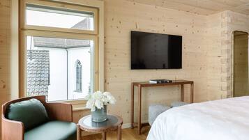 Ein Zimmer mit Holzvertäfelung, einem Bett, einem an der Wand befestigten Fernseher, einem Fenster mit Blick auf ein Gebäude und einem kleinen Tisch mit einer Blumenvase.