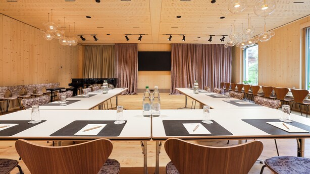Une salle de conférence équipée de longues tables, de chaises, d’un piano et d’un grand écran.