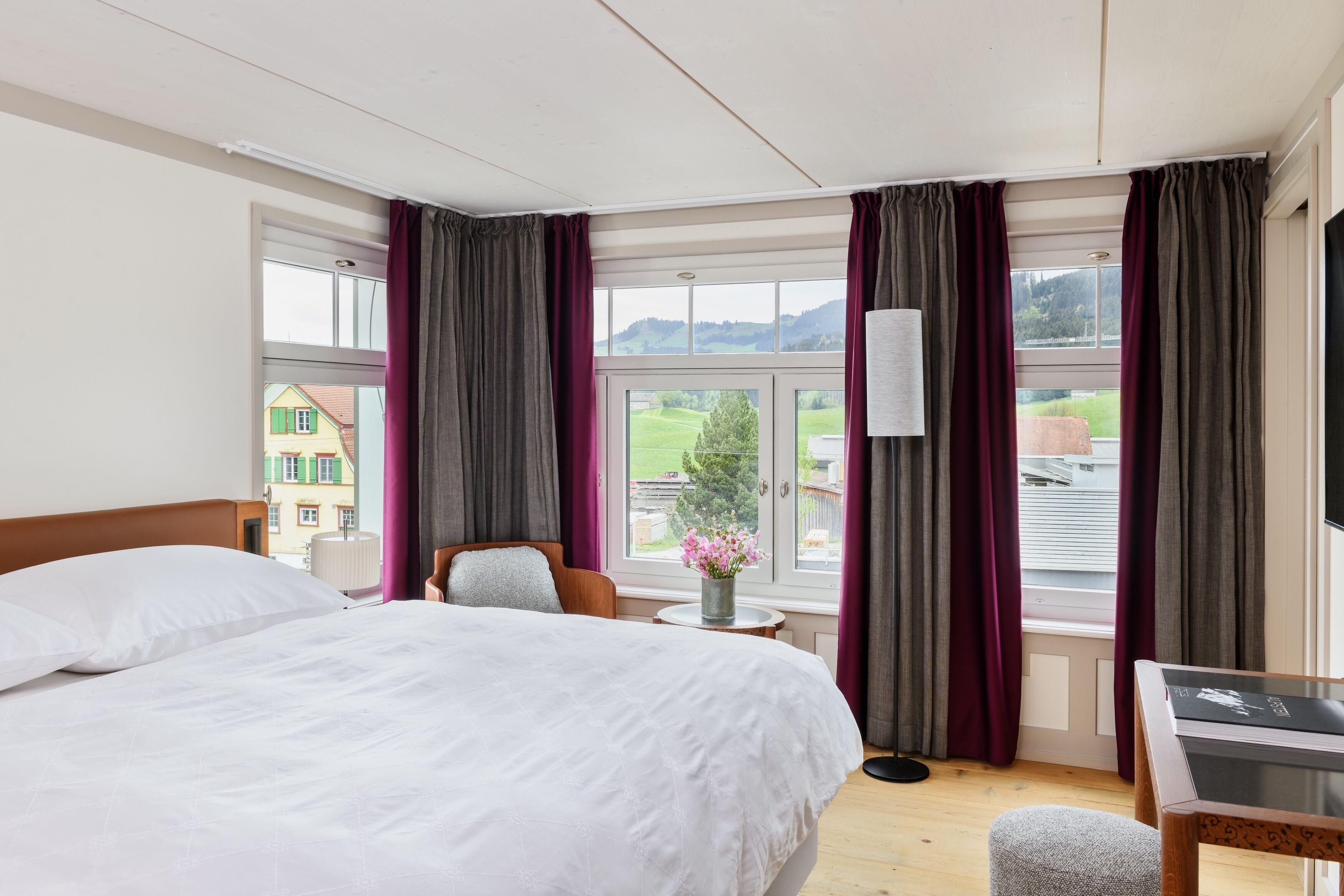 A hotel room with a bed, a desk, a chair, and a view of the outside.