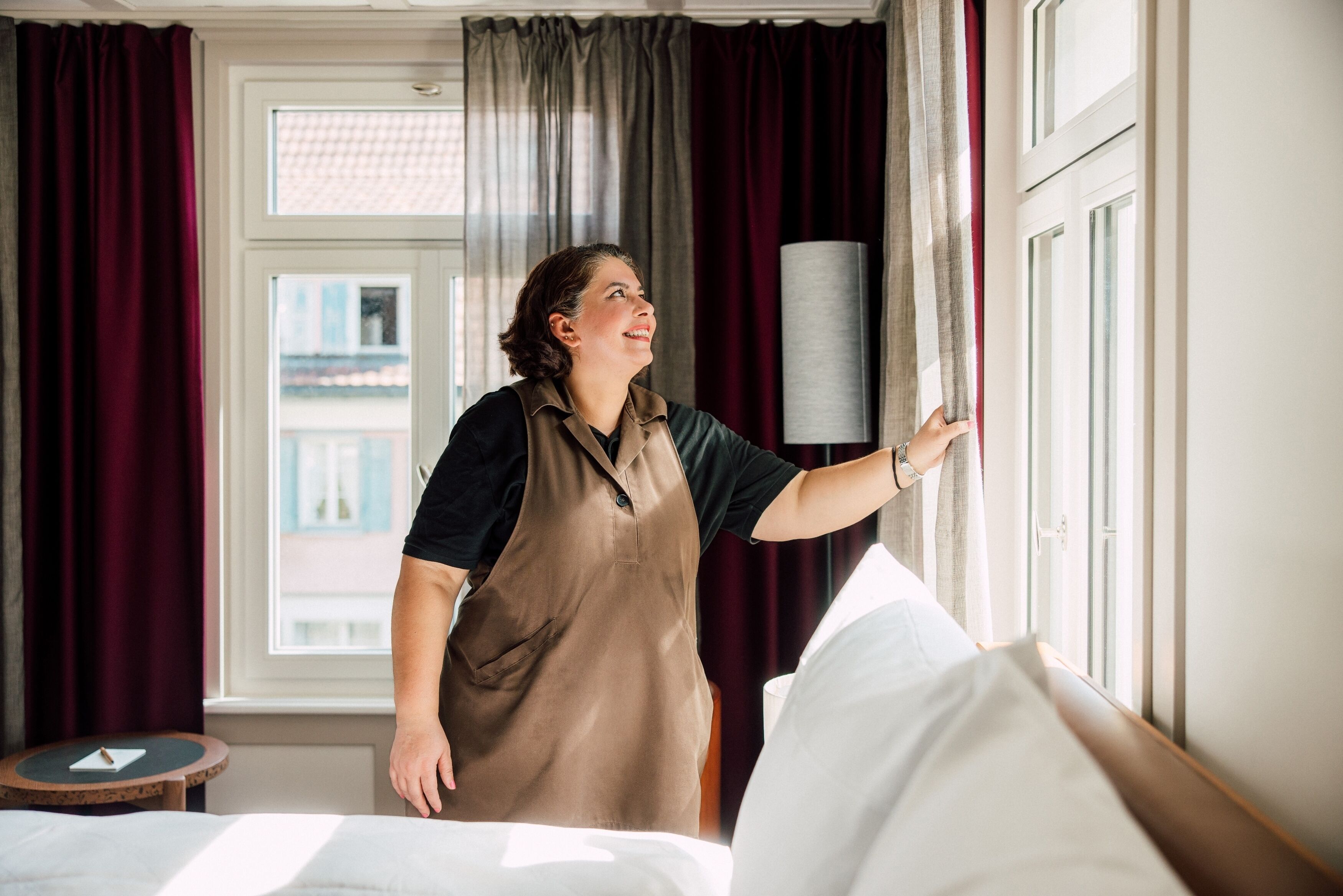 Ein Hotelzimmer mit Bett, einem Fenster mit Vorhängen und einer Lampe auf einem Nachttisch.
