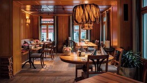 A warmly lit dining area with wooden furniture, a hanging light fixture, and large windows. - HUUS LÖWEN 1878 (Gonten)