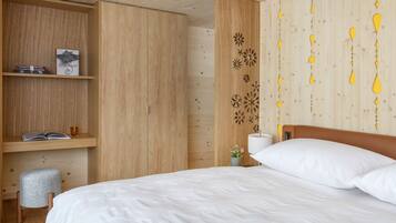 Quarto com guarda-roupa de madeira, mesa de cabeceira com abajur e cama com roupa de cama branca.