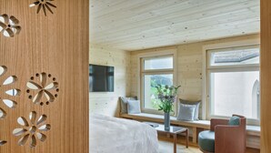 A wooden cabin interior with a bed, seating area, and large windows. - HUUS LÖWEN 1878 (Gonten)