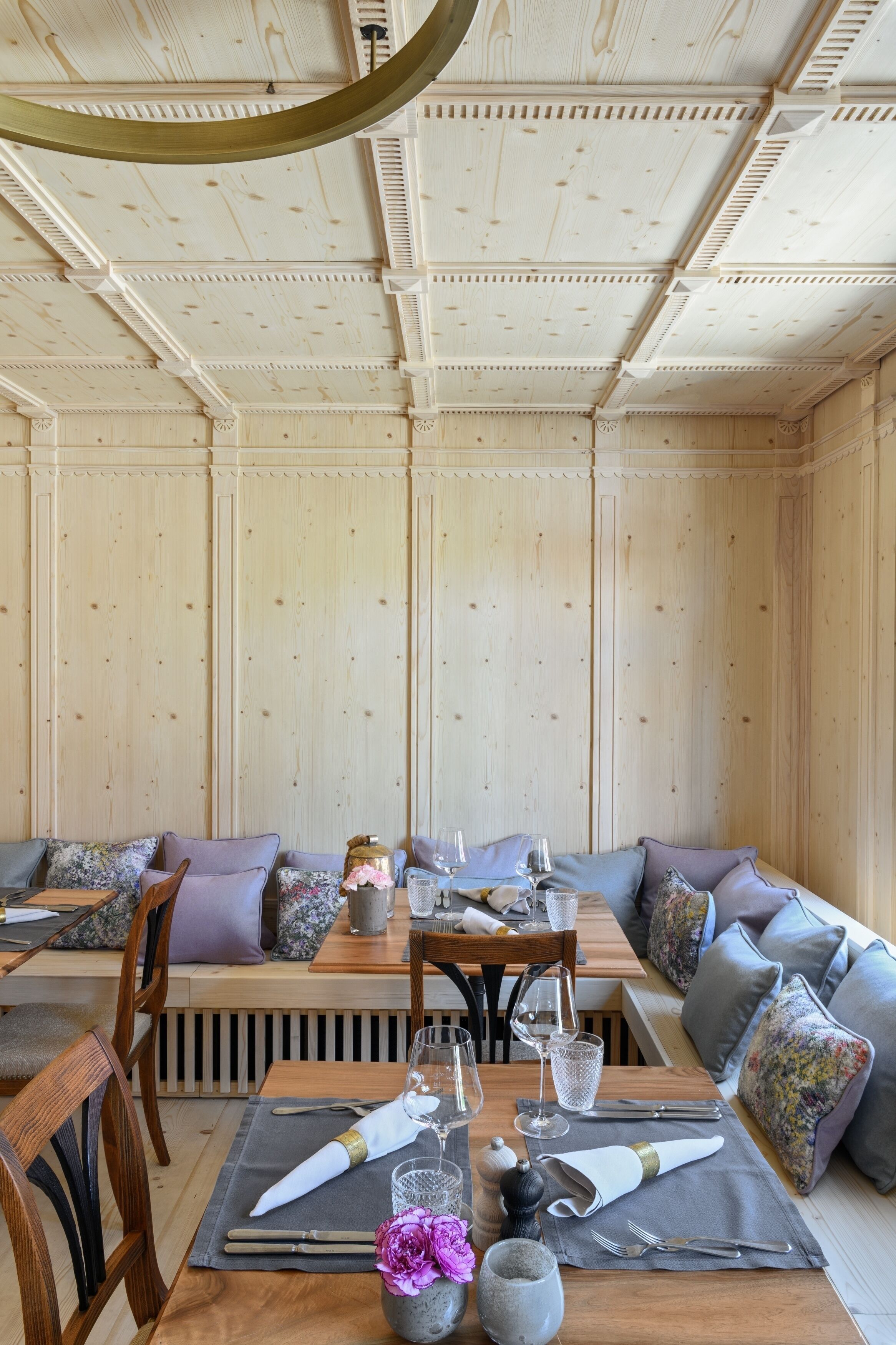 Un comedor con paredes de paneles de madera, techo de madera y una mesa preparada para comer, con sillas y cojines.