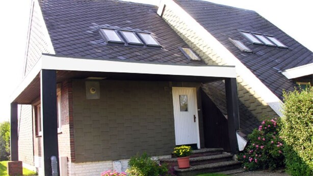 A two-story house with a sloped roof, a front porch, and a small garden with flowers and shrubs. - Vacation home directly on the dike Pet friendly (Wurster Nordseeküste)