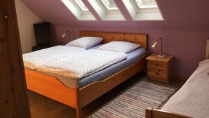 A bedroom with a wooden bed, a nightstand, a lamp, and skylights. - Vacation home directly on the dike Pet friendly (Wurster Nordseeküste)