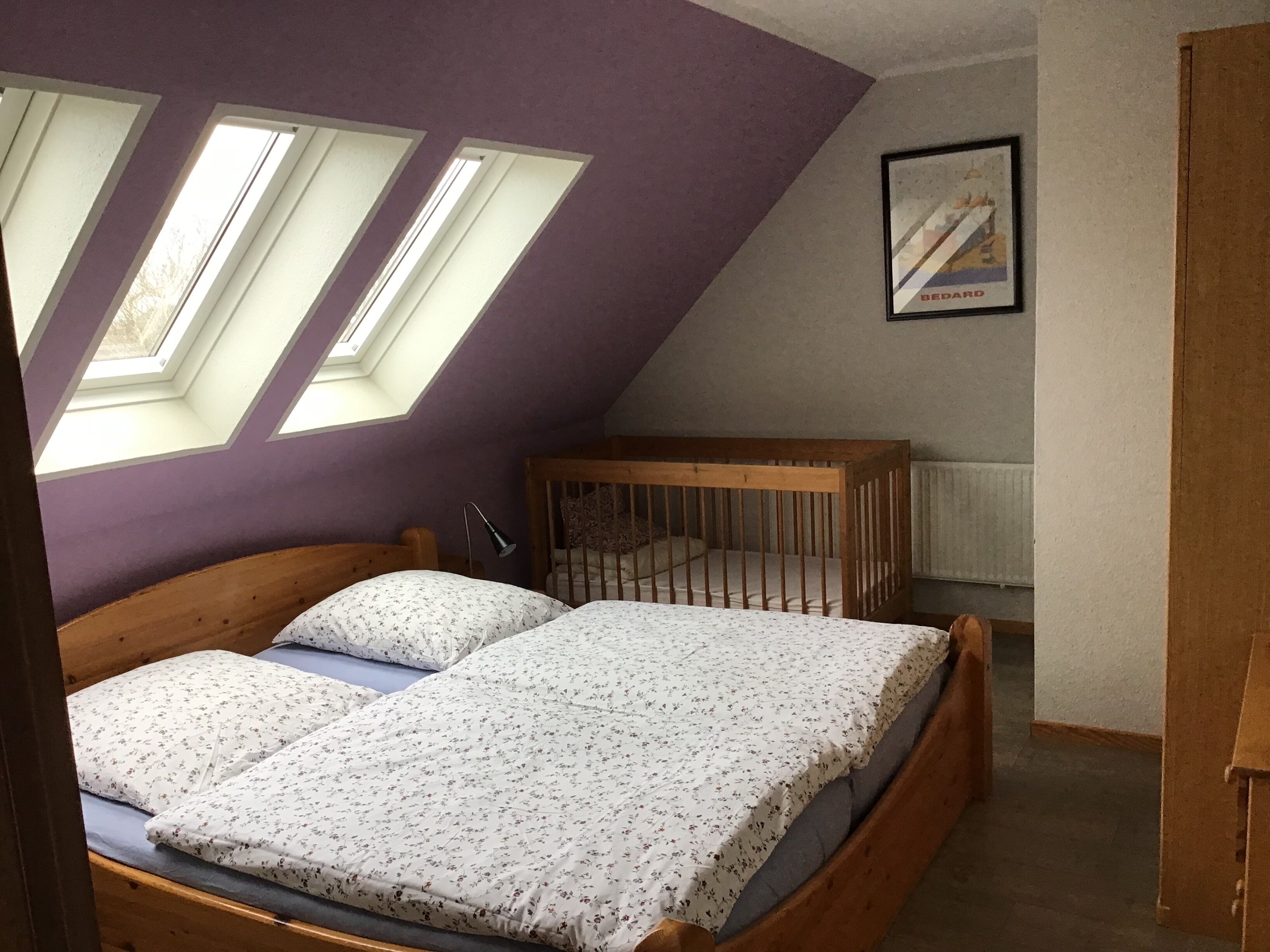 A bedroom with a sloped ceiling, skylights, a crib, and a framed picture on the wall.