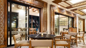 Comedor con mesas y sillas redondas, un detalle decorativo en la pared y vistas al área de estar exterior.