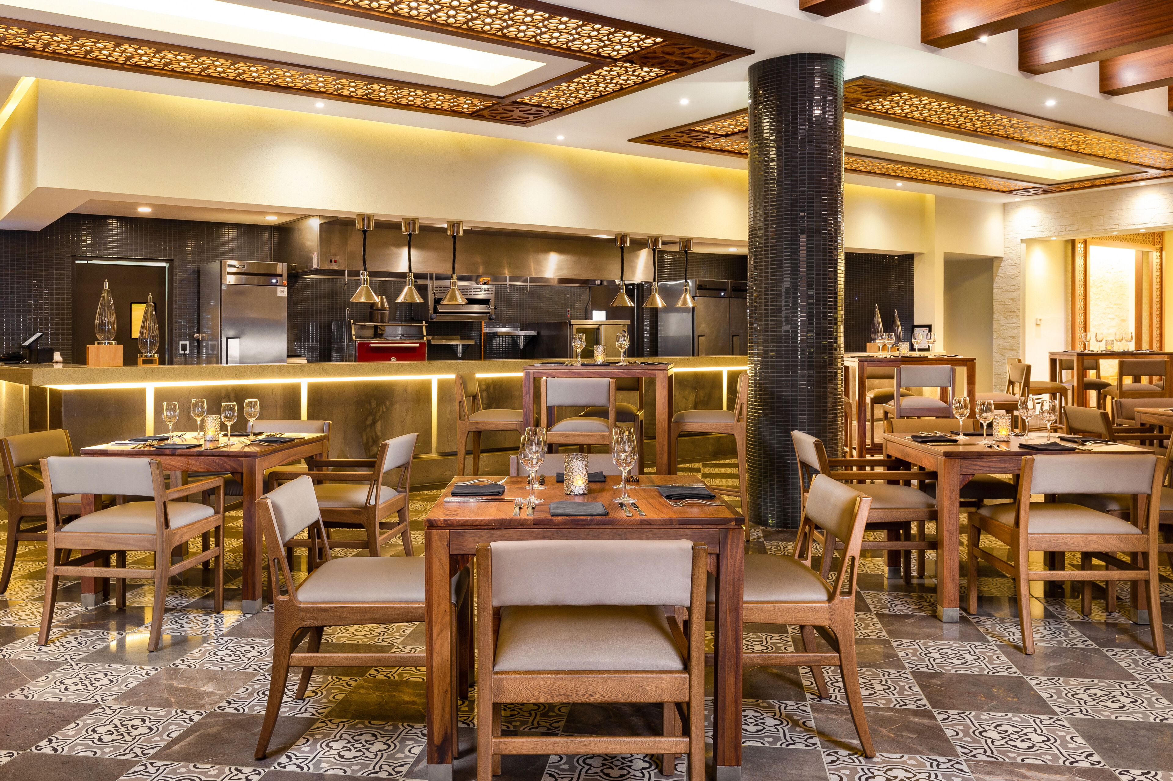Un restaurante moderno con mesas y sillas de madera, una zona de bar y una cocina al fondo.