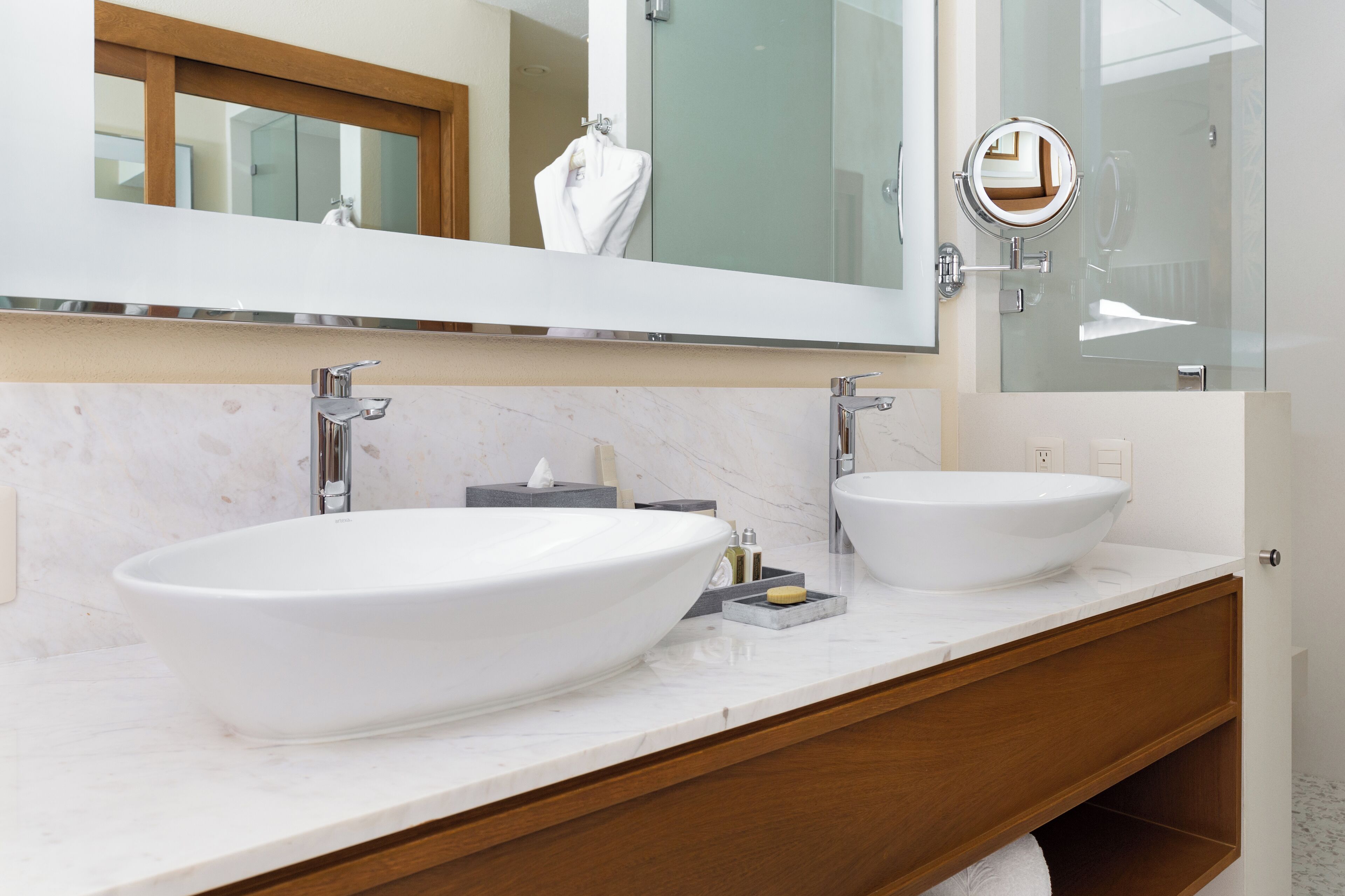 A modern bathroom with two large white sinks, a large mirror, and a wooden vanity.
