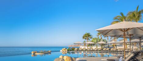 Un espace aménagé au bord de la piscine, avec des chaises longues et des parasols, offrant une vue sur une mer d’un bleu limpide.